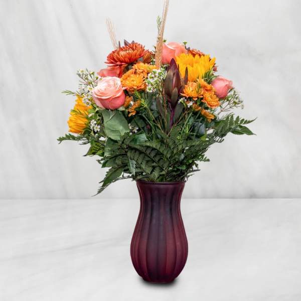 Mixed bouquet of pink, orange, and yellow flowers in a purple vase