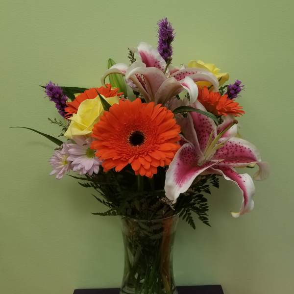 Mixed bouquet with orange gerbera daisies, pink lilies, and yellow roses in a glass vase