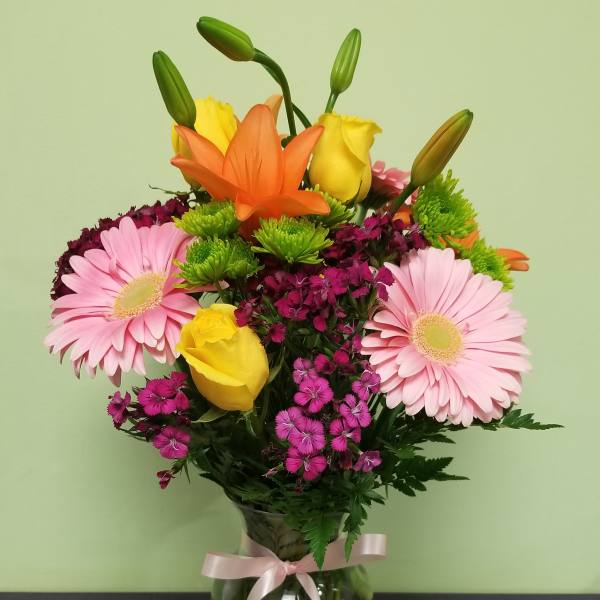 Bouquet of pink gerbera daisies, yellow roses, and orange lilies in a glass vase