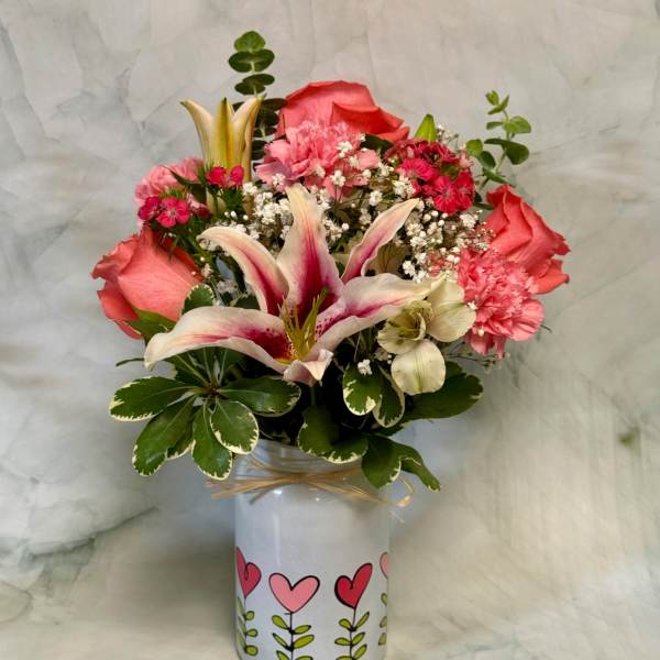 Pink lilies, roses, and carnations arranged in a white vase with heart designs