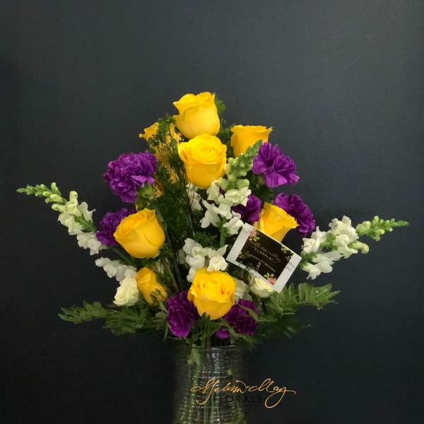 Yellow roses and purple carnations in a clear glass vase