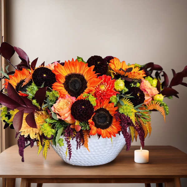 Bright mixed floral arrangement in a white textured bowl with a small candle beside it
