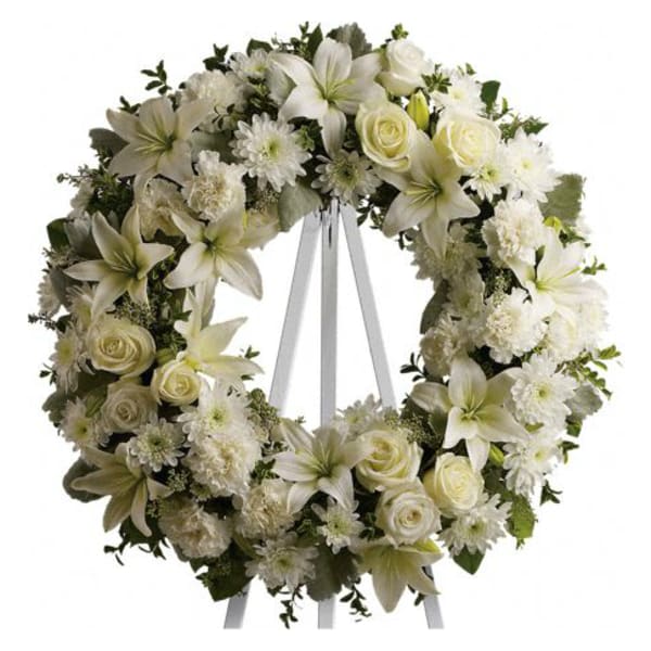 White floral wreath with roses, lilies, and daisies on a ribbon stand