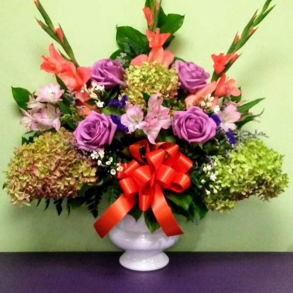 Colorful mixed flower arrangement in a white vase with a red bow