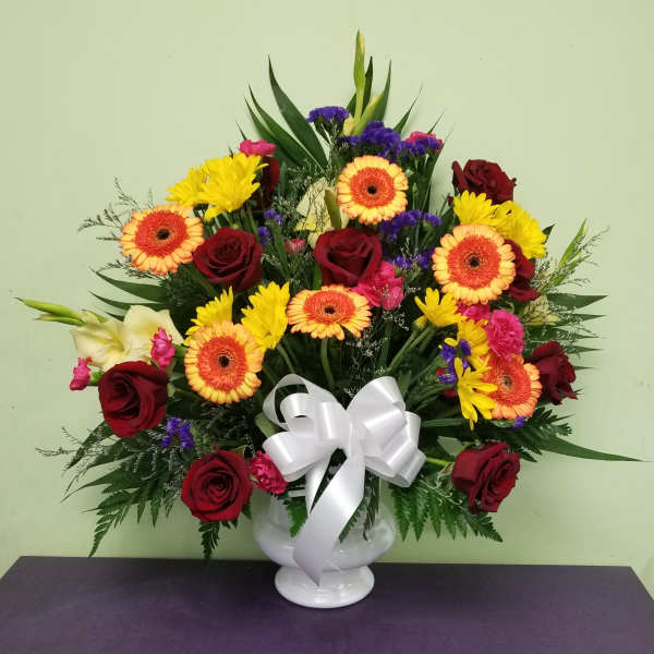 Mixed bouquet of red roses, yellow daisies, and orange gerberas in a white vase