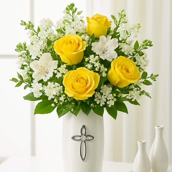 Yellow roses and white flowers arranged in a white vase with a cross emblem