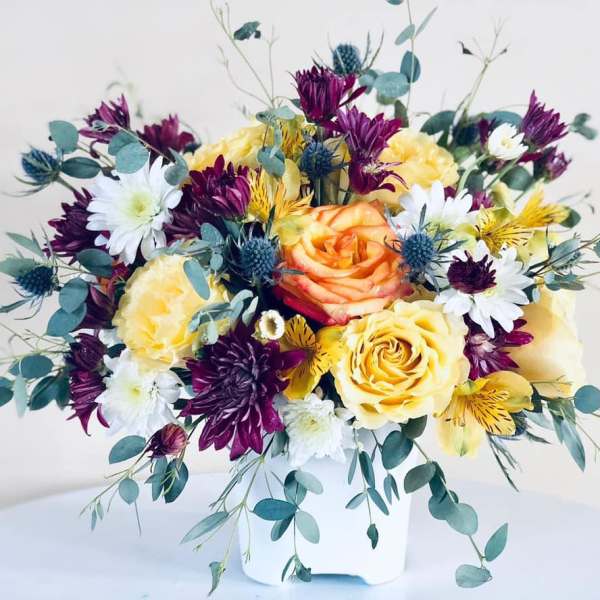 Bouquet of yellow and purple flowers in a white container