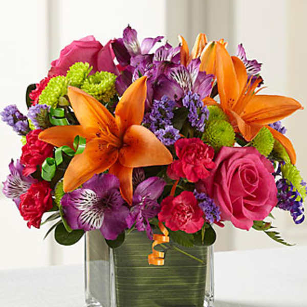 Bright mixed bouquet with orange lilies, pink roses, and purple flowers in a glass vase