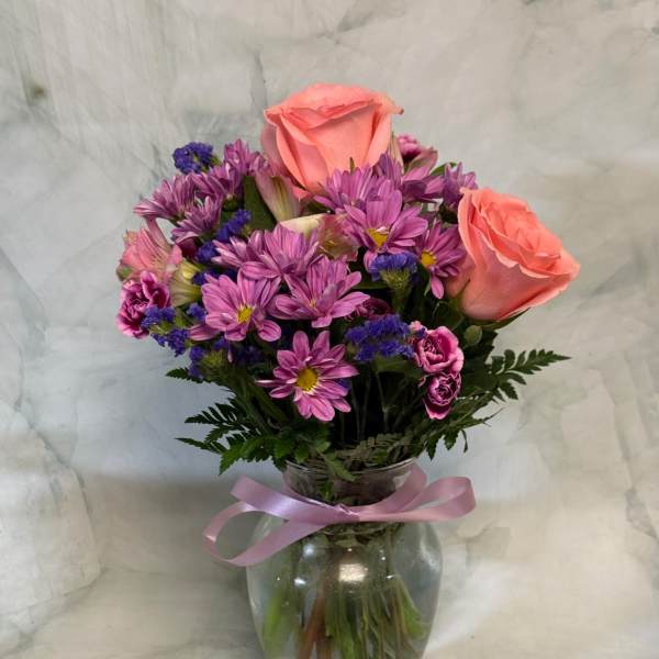 Pink roses and purple daisies in a glass vase with a ribbon
