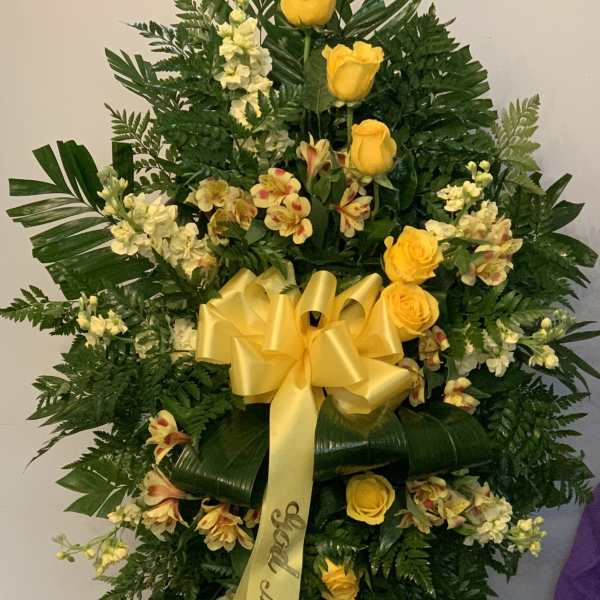 Standing floral spray with yellow roses and white blooms on a ribboned easel