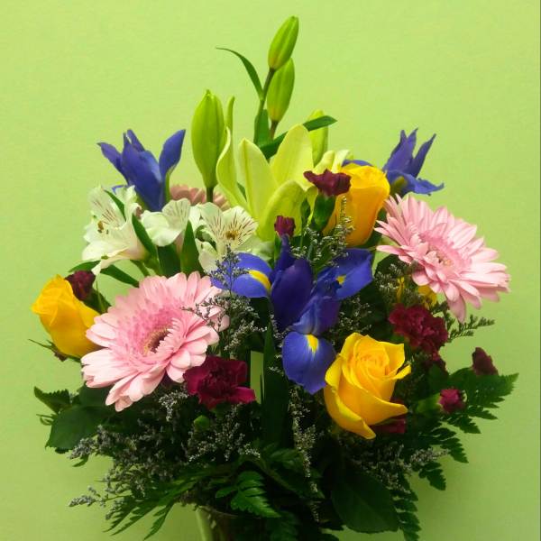 Mixed bouquet of lilies, roses, irises, and gerbera daisies in a glass vase