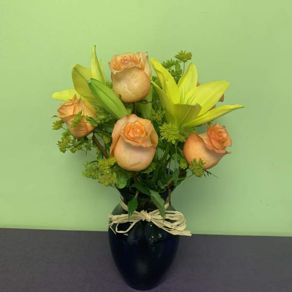 Peach roses and yellow lilies in a black vase with a raffia bow