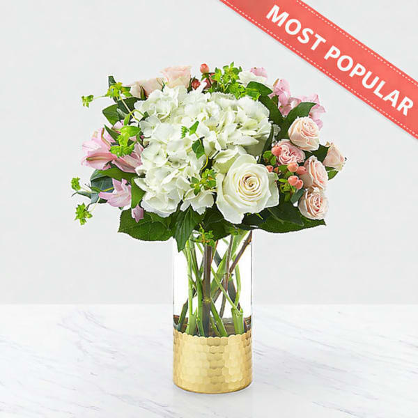 Bouquet of white and pink flowers in a clear glass vase with a gold base