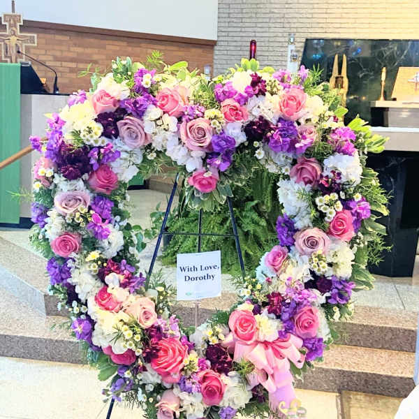 Heart-shaped floral wreath with pink, purple, and white flowers on a stand