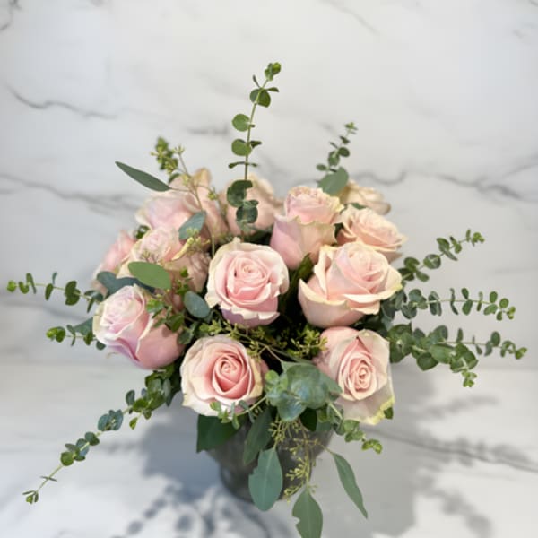 Bouquet of pale pink roses in a dark vase with airy greenery