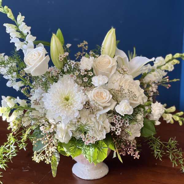 White floral arrangement in a white vase with roses, lilies, and chrysanthemums