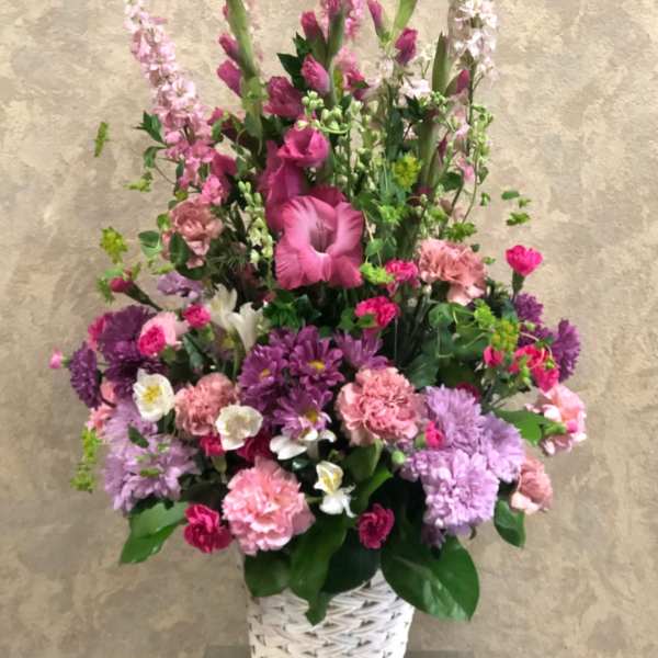 Tall pink and purple floral arrangement in a white woven basket