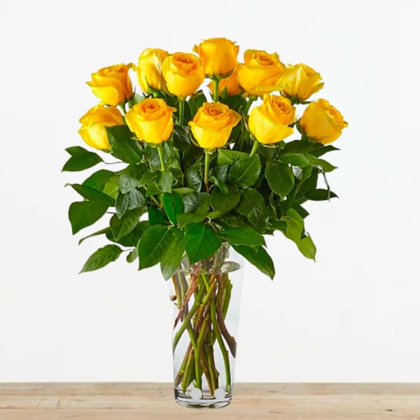Tall arrangement of yellow roses in a clear glass vase on a wooden surface