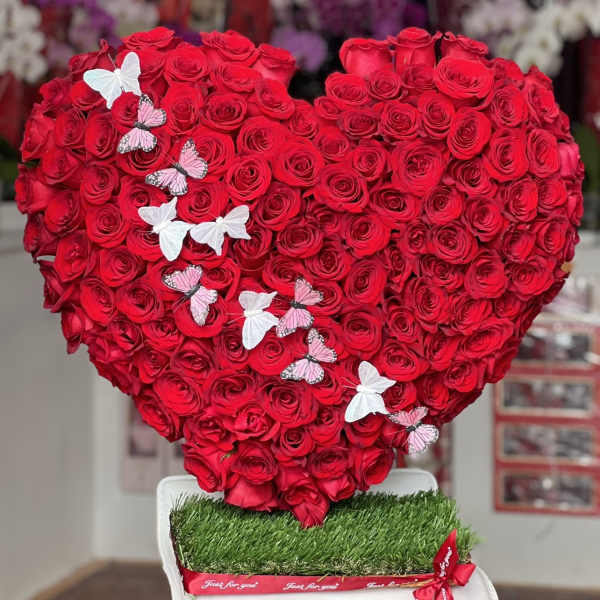 Heart-shaped arrangement of red roses with butterfly decorations on a white stand