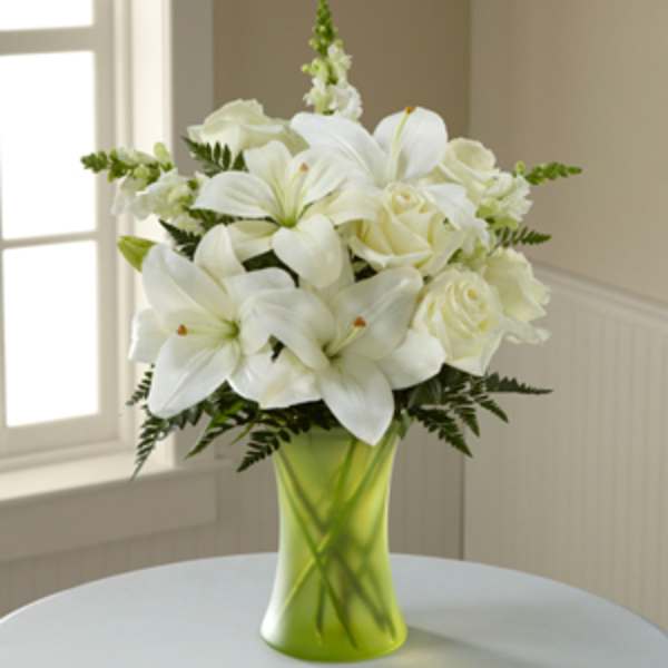 White lilies and roses in a green glass vase