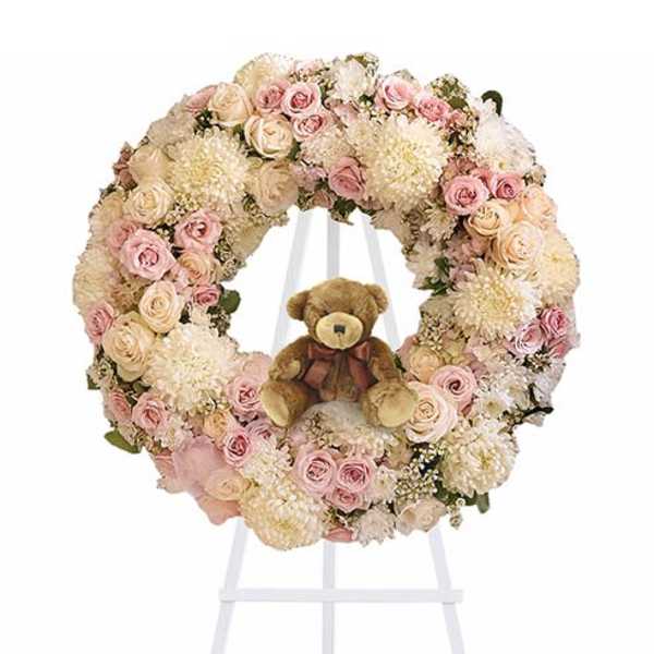 Pastel floral wreath with a teddy bear in the center on a white stand
