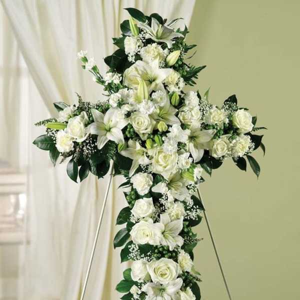 White floral cross on an easel with roses and lilies