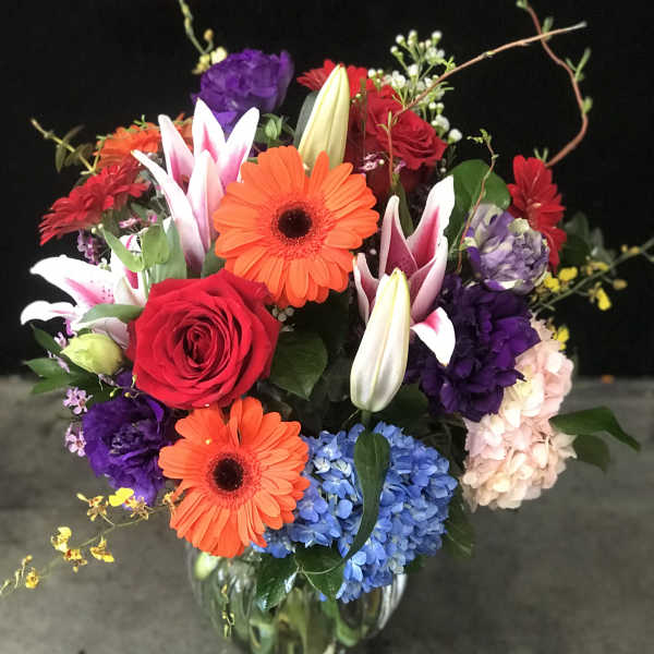 Mixed bouquet of roses, gerbera daisies, lilies, and hydrangeas in a glass vase