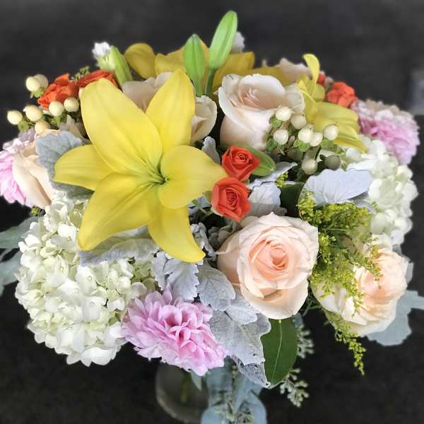 Mixed arrangement with yellow lily, peach roses, white hydrangeas, and pink blooms in a glass vase