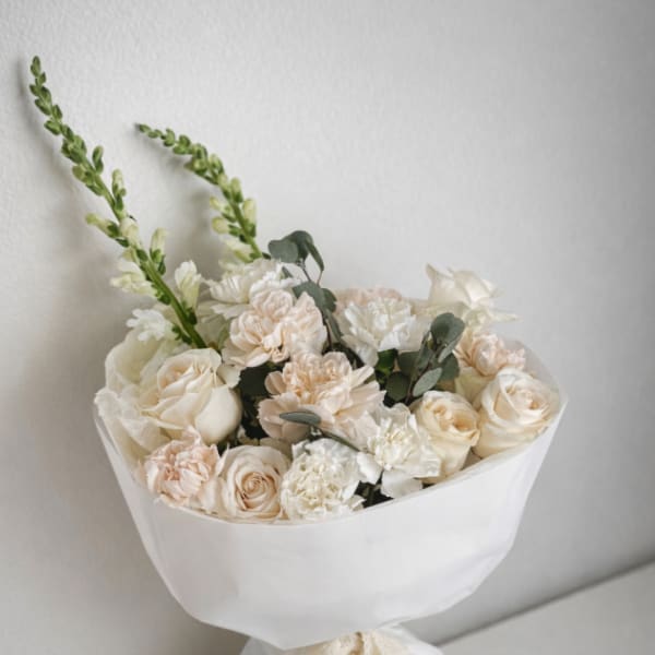 Cream and blush bouquet wrapped in white paper with a lace ribbon