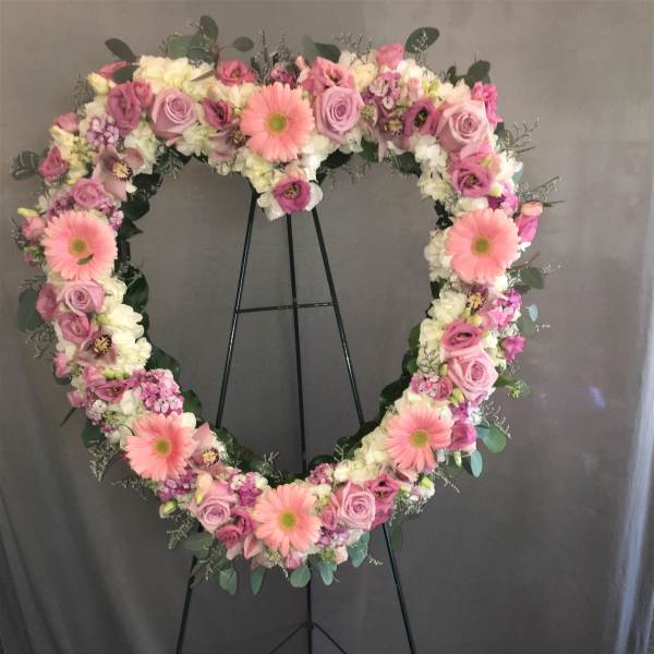 Heart-shaped floral wreath on a black stand with pink and white flowers
