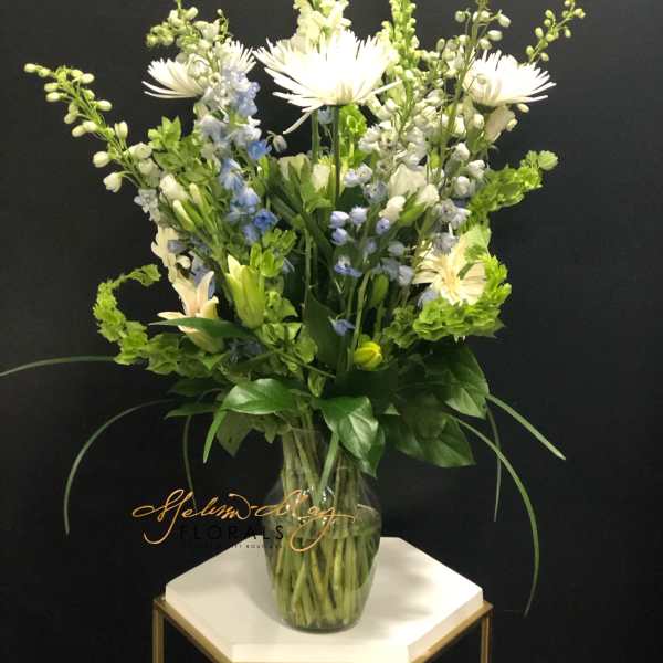 Tall white and blue floral arrangement in a clear glass vase