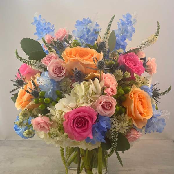 Mixed bouquet of roses, hydrangeas, and blue flowers in a clear glass vase