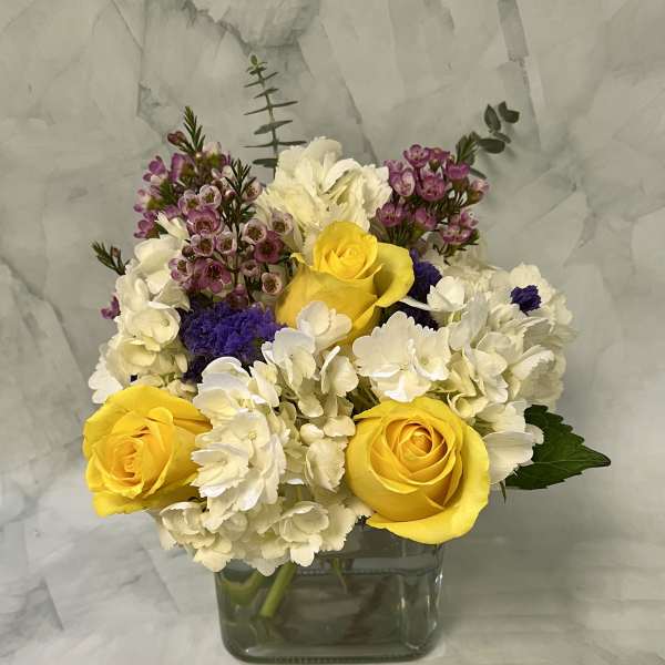 Yellow roses and white hydrangeas in a square glass vase
