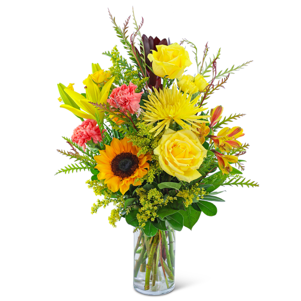 Mixed bouquet of yellow roses, sunflower, lilies, and carnations in a glass vase