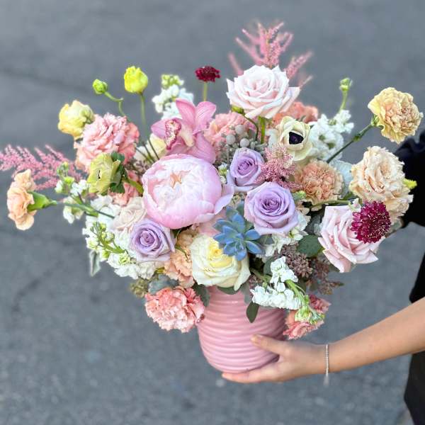 Pastel mixed bouquet in a pink vase with roses, peonies, and orchids