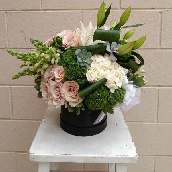 Bouquet of pale pink roses, white lilies, and hydrangeas in a black hatbox
