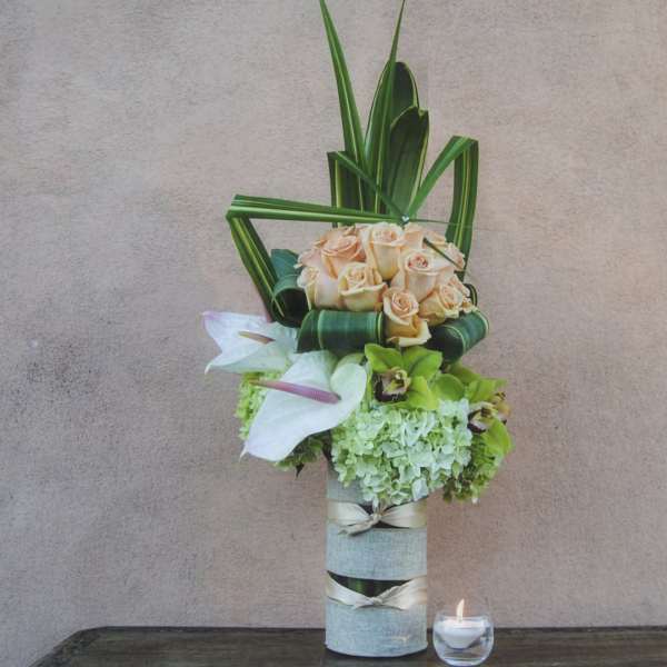 Tall floral arrangement with peach roses and white calla lilies in a wrapped vase