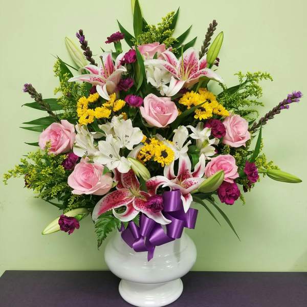Pink roses and lilies in a white vase with a purple ribbon