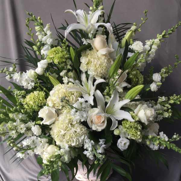 Large white floral arrangement in a basket with lilies and roses