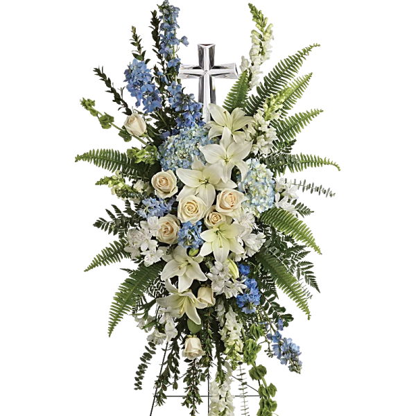 Standing funeral spray with white lilies, cream roses, and blue flowers around a cross
