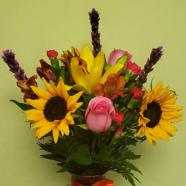 Bouquet of sunflowers, roses, and mixed blooms in a glass vase with an orange ribbon
