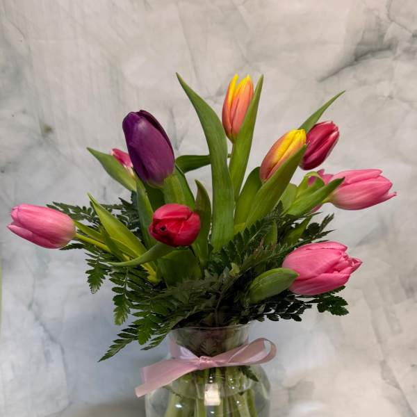 Mixed tulips in a clear glass vase with a pink ribbon