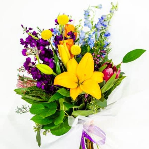 Colorful bouquet with yellow lilies, purple flowers, and blue blooms wrapped in white paper