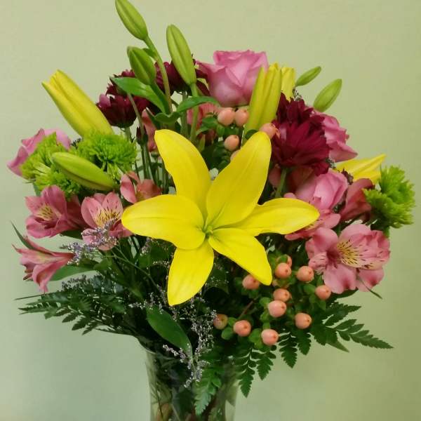 Bouquet of yellow lilies, pink roses, and mixed blooms in a glass vase