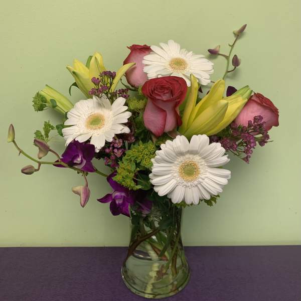 Mixed bouquet of roses, gerbera daisies, lilies, and orchids in a glass vase