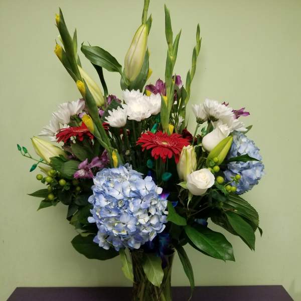 Mixed bouquet in a glass vase with blue hydrangeas, lilies, and gerbera daisies