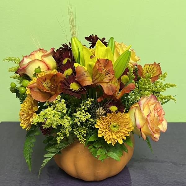 Autumn floral arrangement in a pumpkin-shaped container with roses and lilies