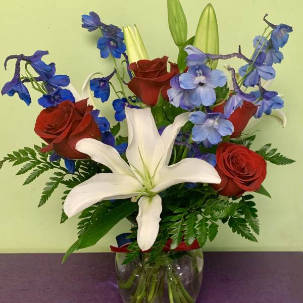 Bouquet of red roses, white lilies, and blue flowers in a glass vase