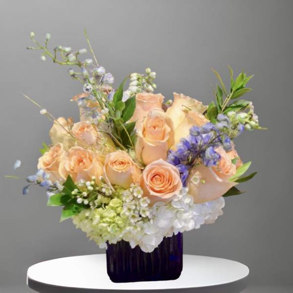Peach roses and blue flowers arranged in a dark vase