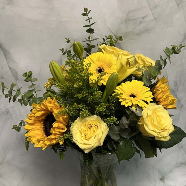 Yellow roses and sunflowers in a clear glass vase